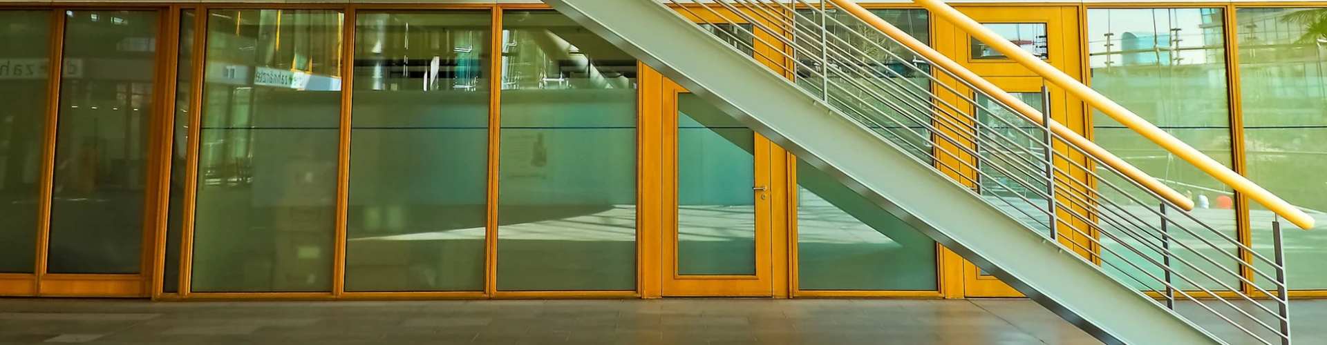 Modern interior view of a building featuring a glass façade and a sleek staircase with yellow handrails.
